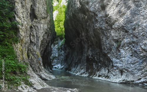 A river flowing through a canyon narrowed by vertical stone walls and sharp cliffs. Water has eroded the calcareous cliffs, forming a tunnel in Ramet gorges, Carpathia, Romania.
