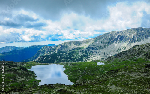 Rainy clouds above the mountain peaks. A glacial lake is in a grassy ravine, and laying in the shadows. Sunlight lits the nearby mountain pastures. Bucura Lake, Carpathia, Romania. © Alexandru V