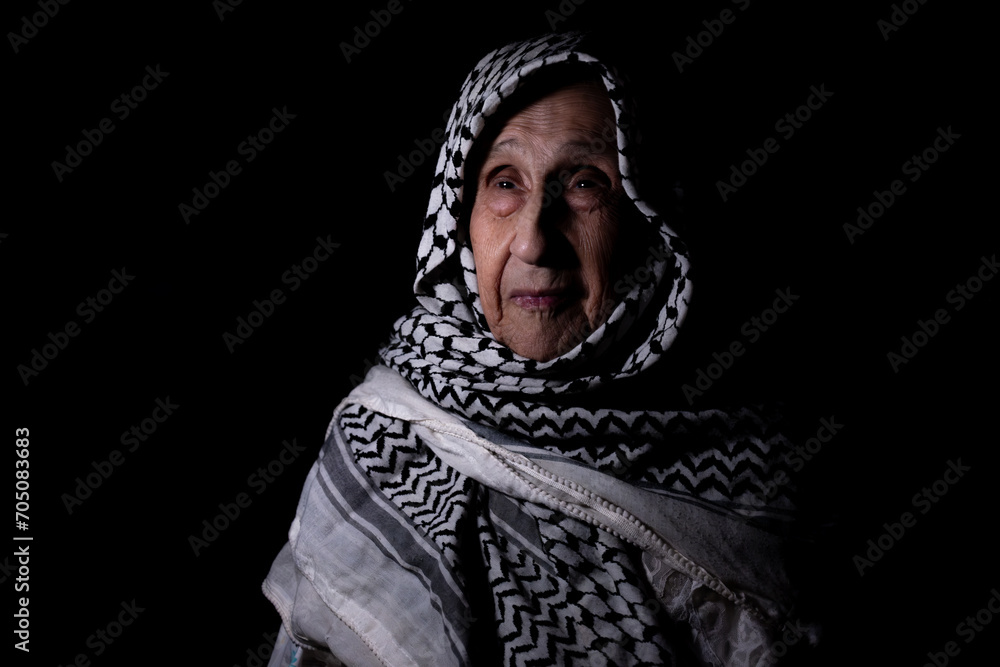 portrait of an old lady in dark background wearing white palestinian keffiyeh with smile on her face looking for freedom and hope to Right of Return for Palestinians