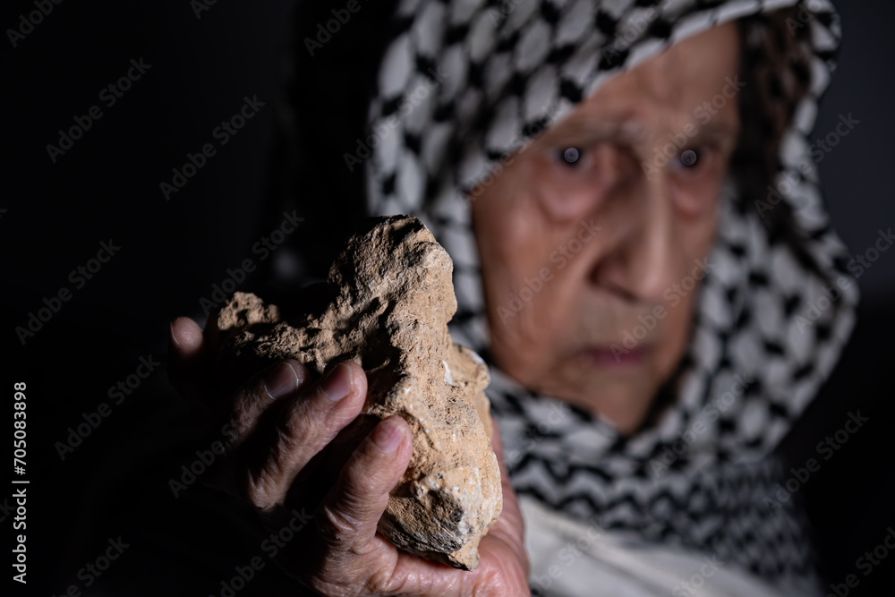 portrait for old woman holding stone which represents the only weapon against the occupation and will be the road to freedom