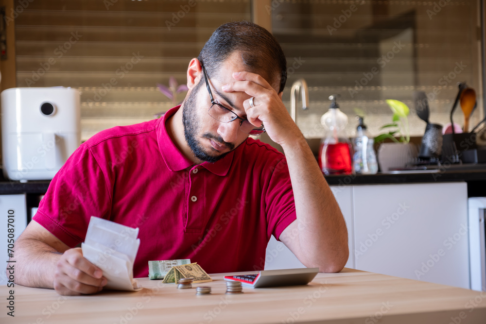 man sitting in the kitchen and calculating the costs of living feeling frustrated man sitting in the kitchen and calculating the costs of living feeling frustrated
