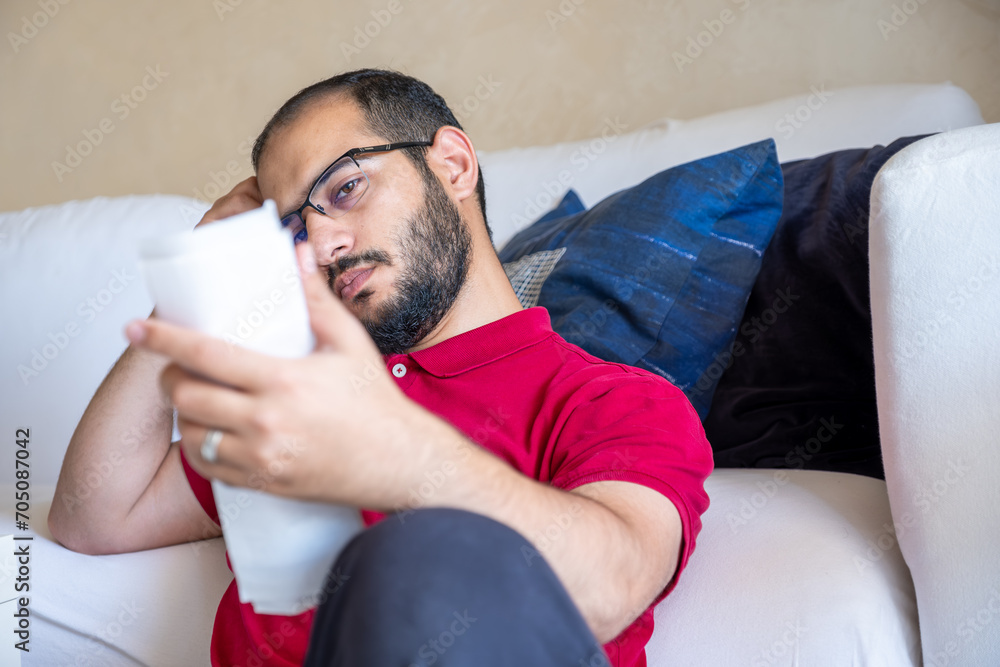man is frustrated from the living costs holding his bill and sitting in front of the couch man is frustrated from the living costs holding his bill and sitting in front of the couch