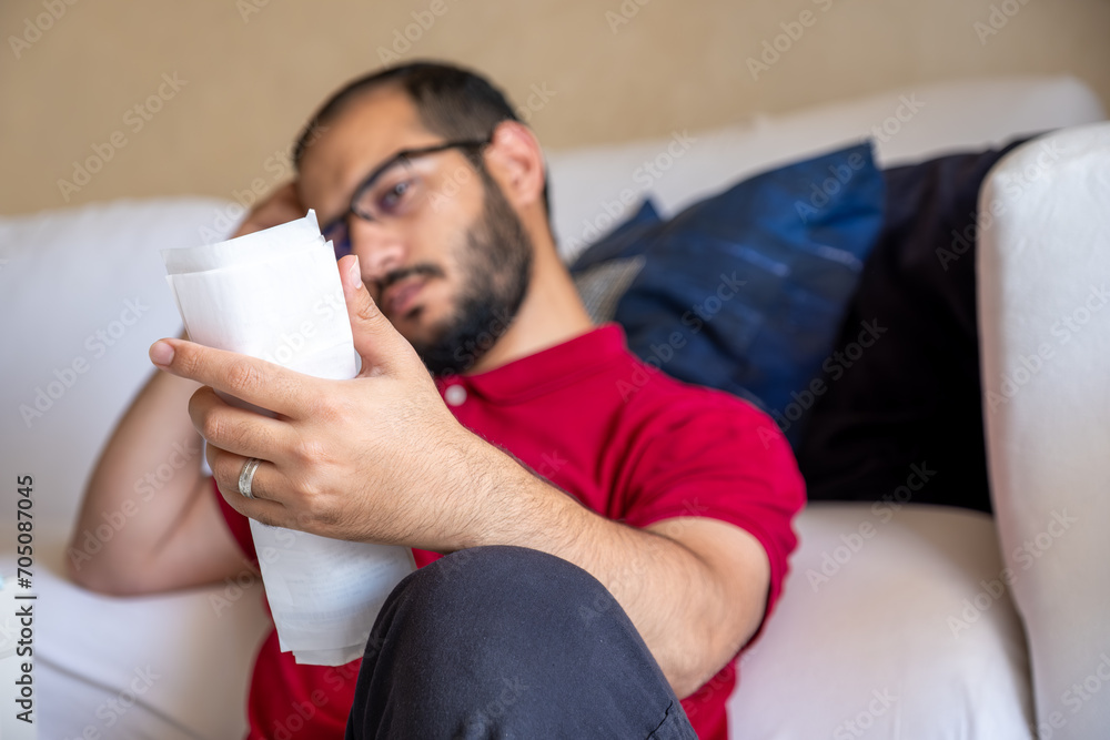 man is frustrated from the living costs holding his bill and sitting in front of the couch man is frustrated from the living costs holding his bill and sitting in front of the couch