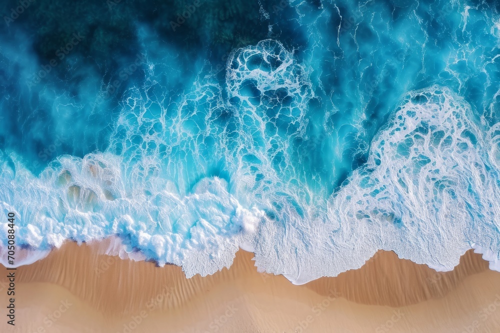 Fototapeta premium Aerial view of ocean waves crashing onto a sandy shore.