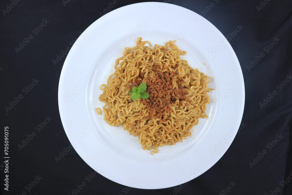 instant fried noodles sprinkled with spices and mint leaves on top, served on a white plate. Top view instant fried noodles sprinkled with spices and mint leaves on top, served on a white plate. Top view