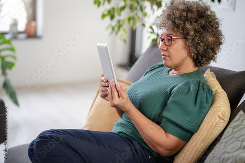 Beautiful middle-aged woman using a computer tablet to read a book and surf internet. Modern technologies used by elderly people. Mature woman using digital tablet at home photo