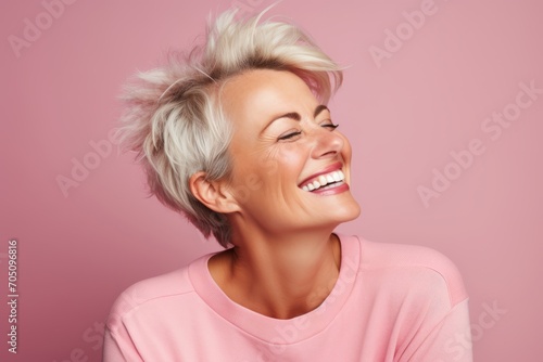 Happy smiling middle aged woman with short blonde hair on pink background.