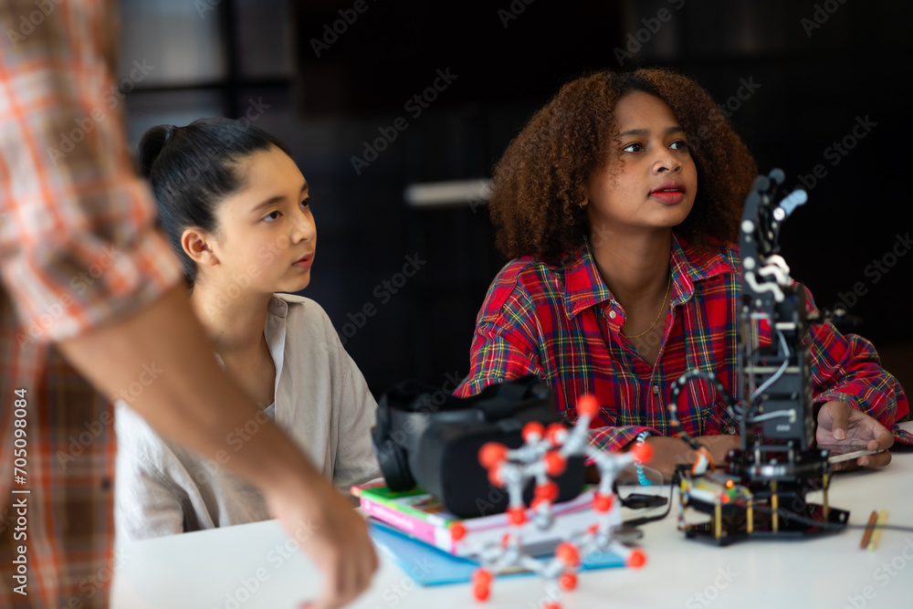 Fototapeta premium Happy african american girl and diverse teens students group building robotic hand using laptop computer. Building And Learning To Program electric Robot. STEM coding engineering class.