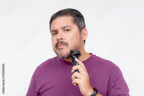 A middle aged man using a cordless trimmer to shape and trim his beard. Facial care and grooming. Looking at camera, isolated on a white background. photo