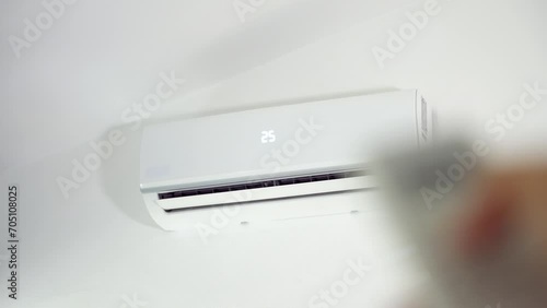 Close up of man turns on the white air conditioner at 25 degrees on the wall with the remote control inside the living room. Comfortable temperature in the bedroom during hot weather photo