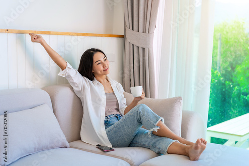 Young woman relaxing at cozy home atmosphere and look out the window on sofa with cup of coffee in the morning