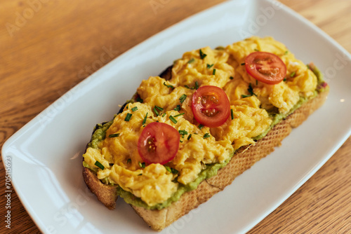Top view of a scrambled eggs on a toast, with a pesto sauce and tomatoes on the top.