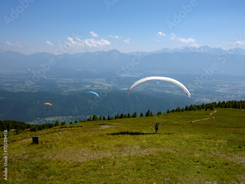 Gleitschirmflieger über grüner Almwiese in Kärnten mit Alpenpanorama
