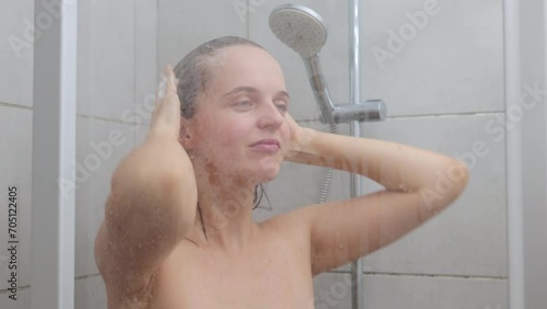 Hygienic routine. Skin-pampering. Personal care. Showering bliss. Attractive young adult Caucasian brown haired woman with bare shoulders showering through the bath screen photo