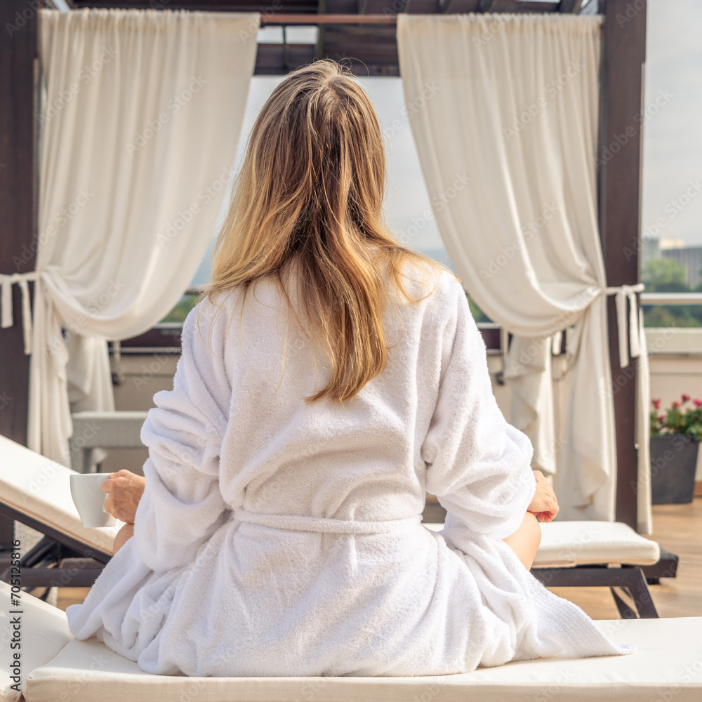 Woman in white bathrobe lying on sofa and relaxing with orange cocktail at the roof. Woman in white bathrobe lying on sofa and relaxing with orange cocktail at the roof.