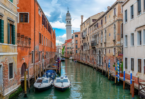 Narrow canal with boats and leaning bell tower in Venice, Italy. Architecture and landmark of Venice. Cozy cityscape of Venice.