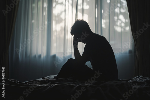 Silhouette of a depressed man sitting sadly on the bed in the bedroom