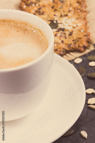 Cup of coffee with milk and fresh baked oatmeal cookies with honey and healthy seeds. Delicious crunchy dessert