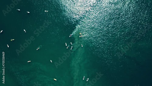 Aerial view captures surfers at popular ocean lineup waiting for waves. Action-packed surf spot showcases individuals paddling, bracing for ride. Drone footage reveals busy water sports. photo