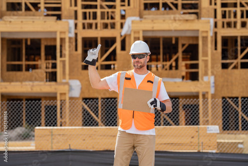 roofer builder working on roog structure of building on construction site. handsome young male builder in hard hat smiling at camera. Construction Worker on Duty. Contractor and the Wooden House Frame