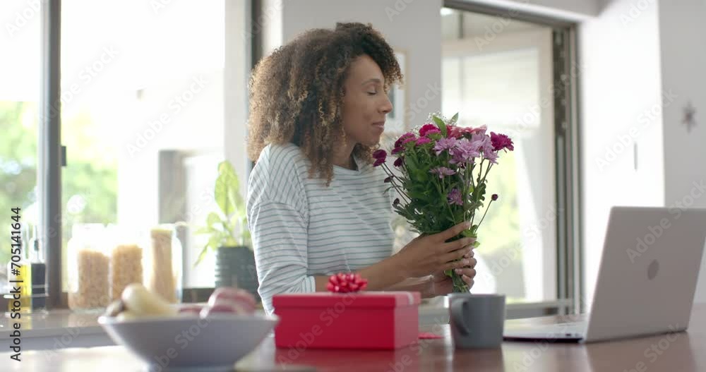 Happy biracial woman with gift and flowers having video call on laptop at home, slow motion Happy biracial woman with gift and flowers having video call on laptop at home, slow motion