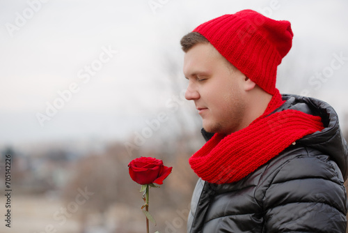 A man in a red hat and scarf is holding a red rose