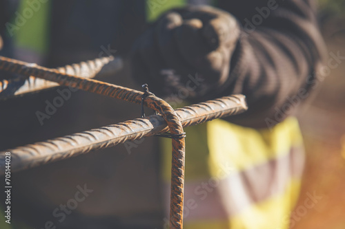 A worker uses steel tying wire to fasten steel rods to reinforcement bars close-up. Reinforced concrete structures - making a steel reinforcing cage for concrete beam photo