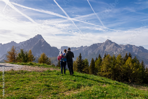 Happy family with baby enjoying scenic view from lift station on mount Helm (Monte Elmo), Carnic Alps, Austria Italy border. Looking at majestic mountain range of untamed Sexten Dolomites, South Tyrol © Chris