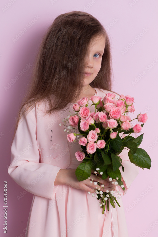 A cute little girl in a pink dress holds a bouquet of pink roses