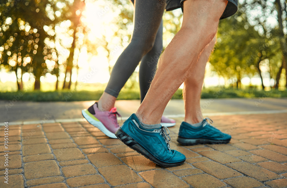 Heathy and active lifestyle. Close up of male and female legs in blue and pink sneakers jogging on cobblestones path at summer park. Caucasian aged couple spending morning time for outdoors activity.