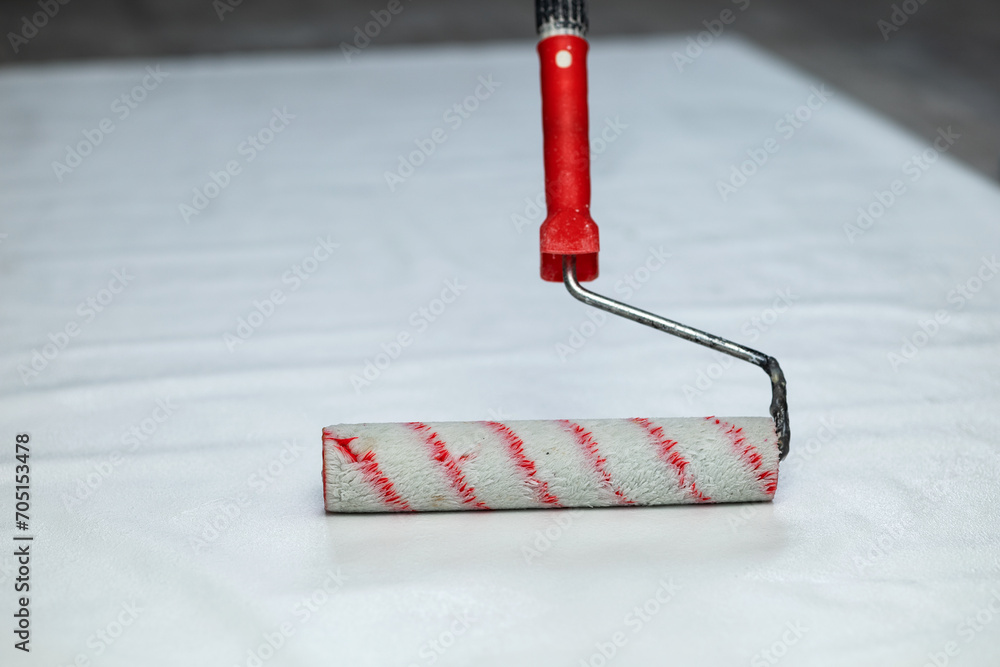 A white paint roller with a red handle. Applying glue to wallpaper - obrazy, fototapety, plakaty 