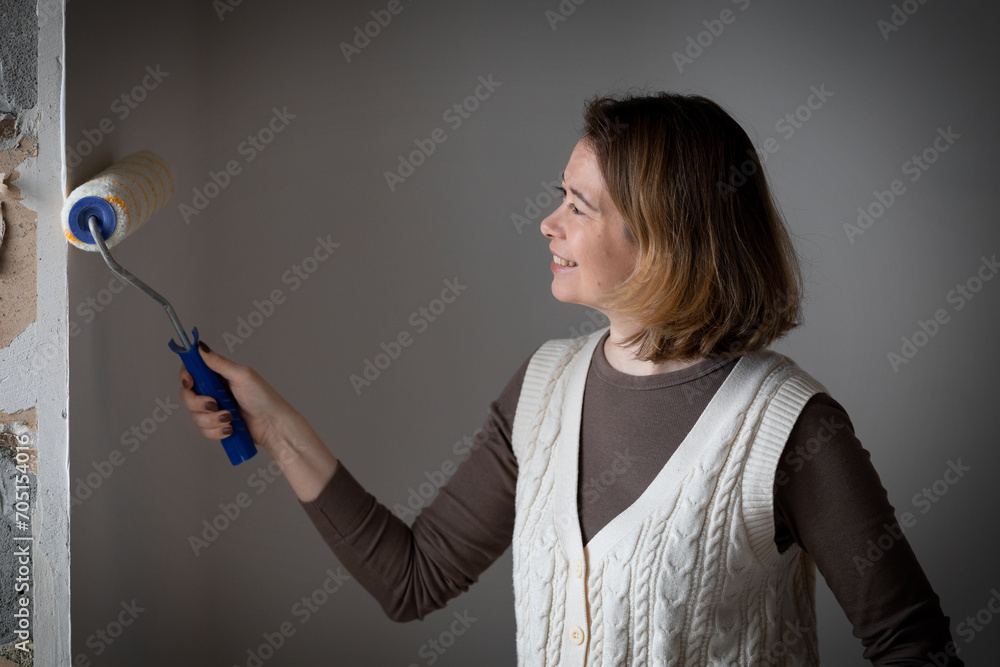 a middle-aged woman applies glue to the wall by the window with a roller for wallpapering a middle-aged woman applies glue to the wall by the window with a roller for wallpapering