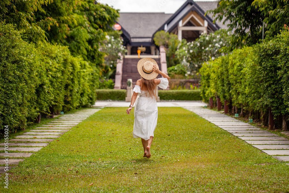 Woman in white dress walking along garden path. Summer relaxation.