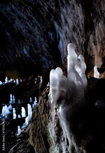 Ice formations in a cave in Sauerland Germany on a very cold winter morning. Bright ranslucent crystalline stalagmites on rocky ground backlit by daylight flashing into the dark limestone cave.  photo