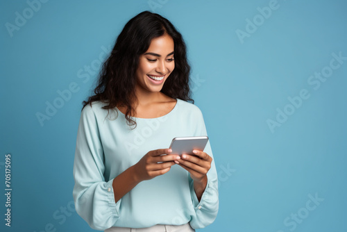 "A cheerful and content young Latin woman smiles as she engages with her smartphone, possibly browsing trendy apps or conducting e-commerce activities. Her focus on the mobile screen indicates she mig