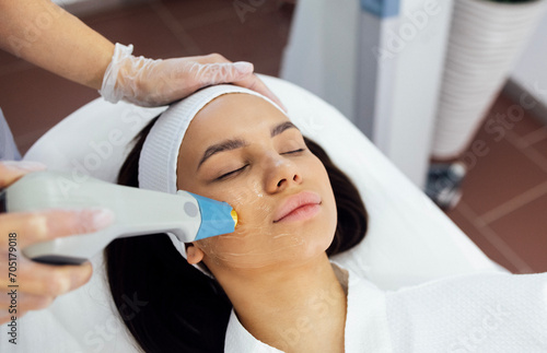 Cosmetologist in grey uniform and transparent gloves makes facial cleansing procedure for her young client