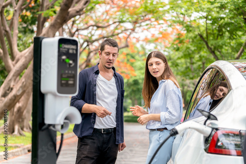 Lovely young couple recharging battery for electric car during autumnal road trip travel EV car in autumnal forest. Eco friendly travel on vacation during autumn. Exalt © Summit Art Creations