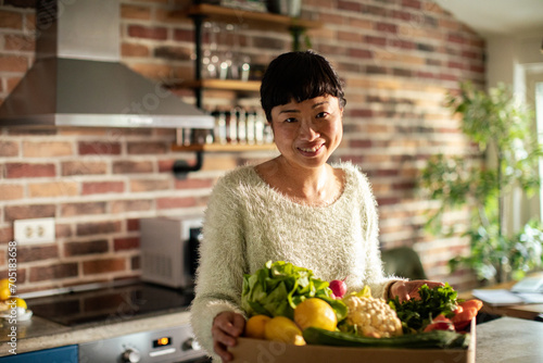 Portrait of a smiling woman with fresh vegetables in kitchen