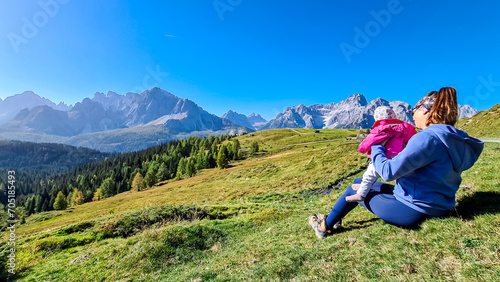 Loving mother holding baby on alpine meadow with scenic view of Sextner Rotwand, Sexten Dolomites, South Tyrol. Idyllic landscape on Klammbachalm (Malga Klammbach), Italian Alps. Tranquil atmosphere