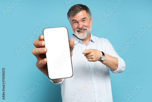 Handsome Excited Mature Man Showing Pointing At Empty Smartphone Screen Posing Over Light Blue Studio Background, Smiling To Camera. Check This Out, Cellphone Display Mock Up photo