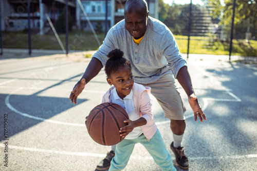 Grandfather teaching granddaughter to play basketball on outdoor court photo