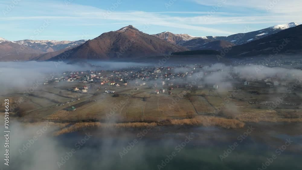 A drone flies over a mountain village covered in morning fog