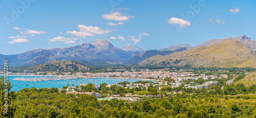 Panoramic view of Port de Pollença, nestled by the Serra de Tramuntana, with azure waters and a vibrant marina - a gem in Mallorca's crown.