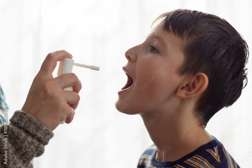 Obraz premium The child receives medication through a mouth spray for a sore throat