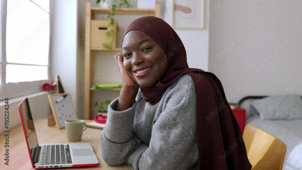 Portrait of young african creative woman smiling at camera sitting at desk. Happy black female student in muslim headscarf relaxing at home. Youth and technology concept. High quality 4k footage Portrait of young african creative woman smiling at camera sitting at desk. Happy black female student in muslim headscarf relaxing at home. Youth and technology concept. High quality 4k footage