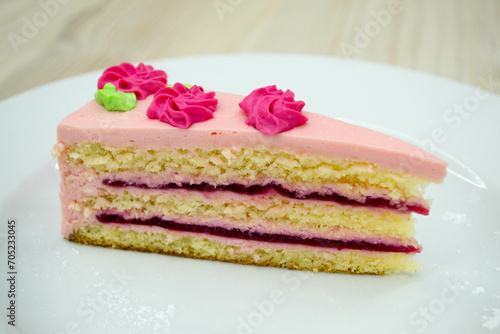 Sweet dessert piece of cake with pink cream and fruit filling with shortbread on a white plate.