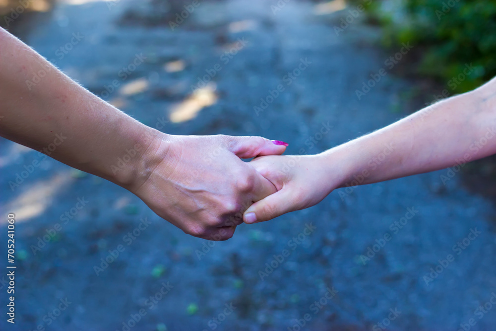 Close up view of mother and daughter holding their hands in the public park. Mothers love