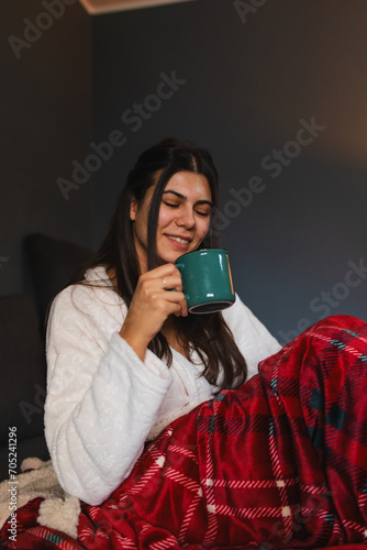 A young girl or woman getting up from bed drinking coffee or tea in blanket cozy room 