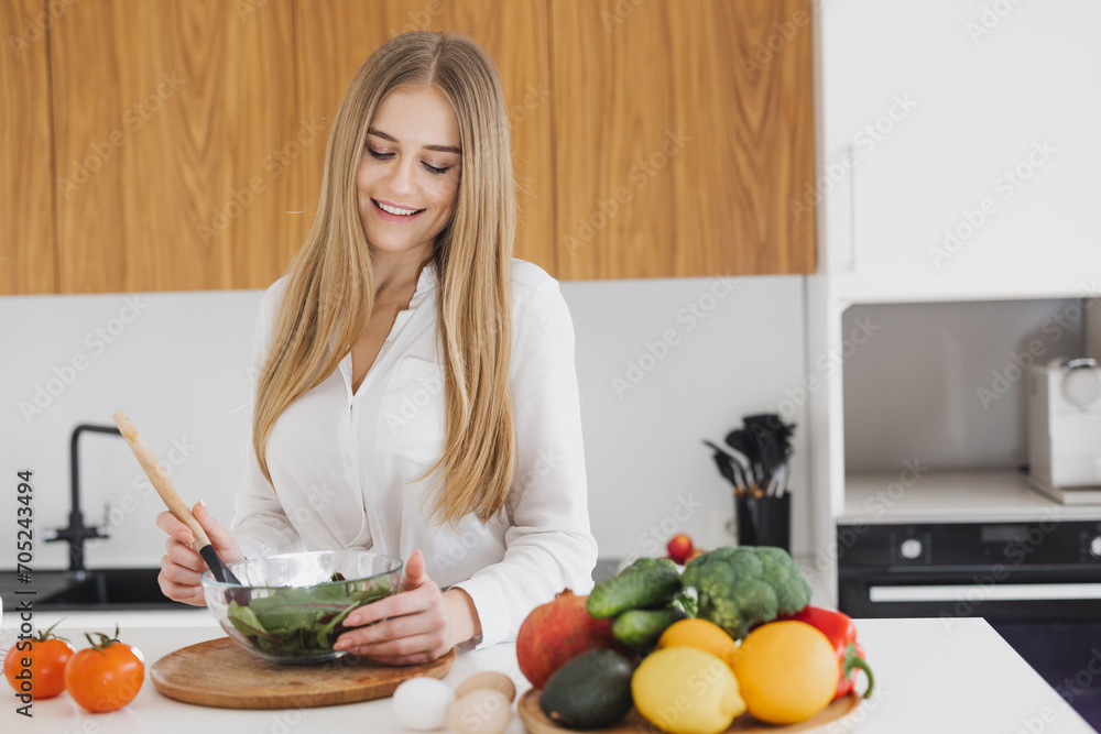 A happy cute blonde woman is preparing a salad in the kitchen A happy cute blonde woman is preparing a salad in the kitchen