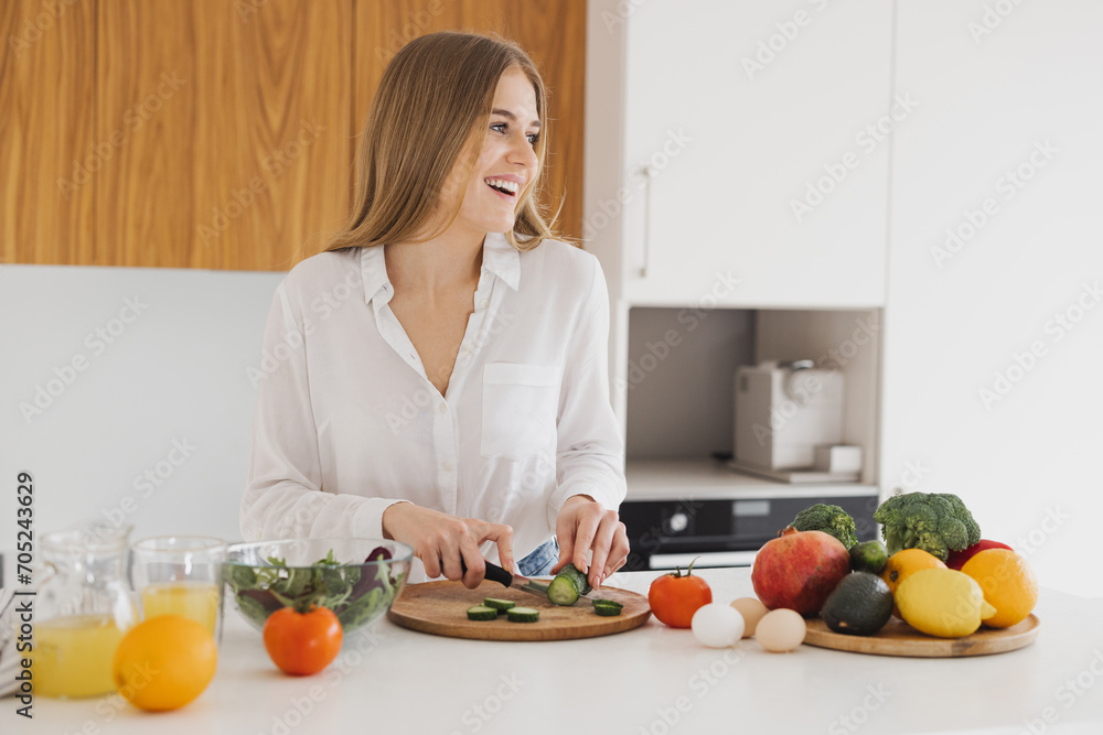 A happy cute blonde woman is preparing a salad in the kitchen A happy cute blonde woman is preparing a salad in the kitchen